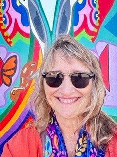 Robbin Robertson smiling in front of a colorful butterfly mural