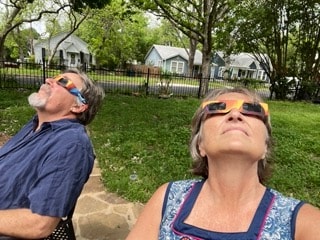 Two people lying in the grass wearing eclipse glasses watching the 2024 solar eclipse