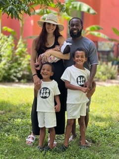 Family portrait outdoors — parents with three young children smiling