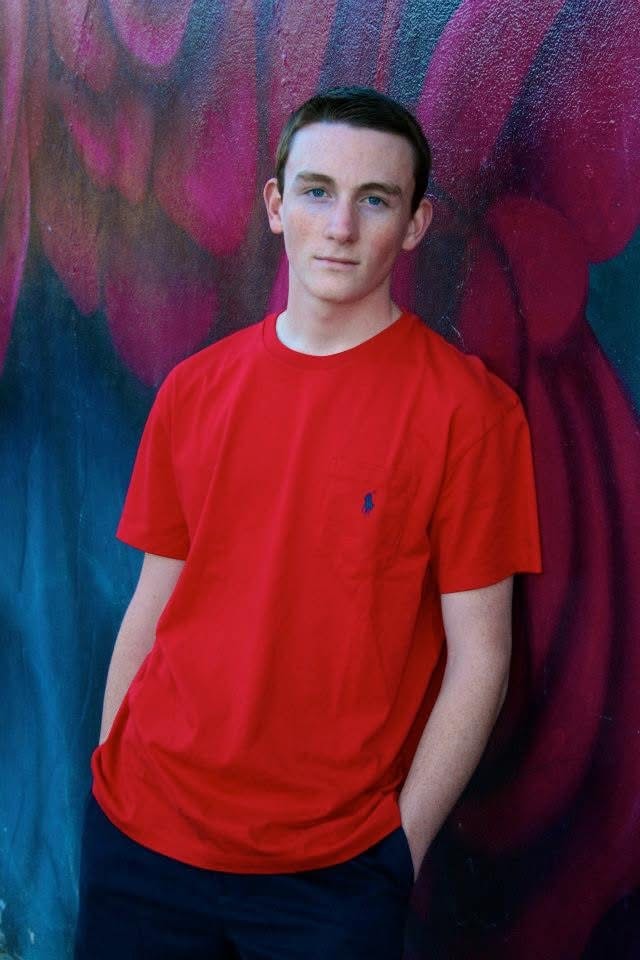Teenage boy in red shirt standing in front of a colorful abstract mural
