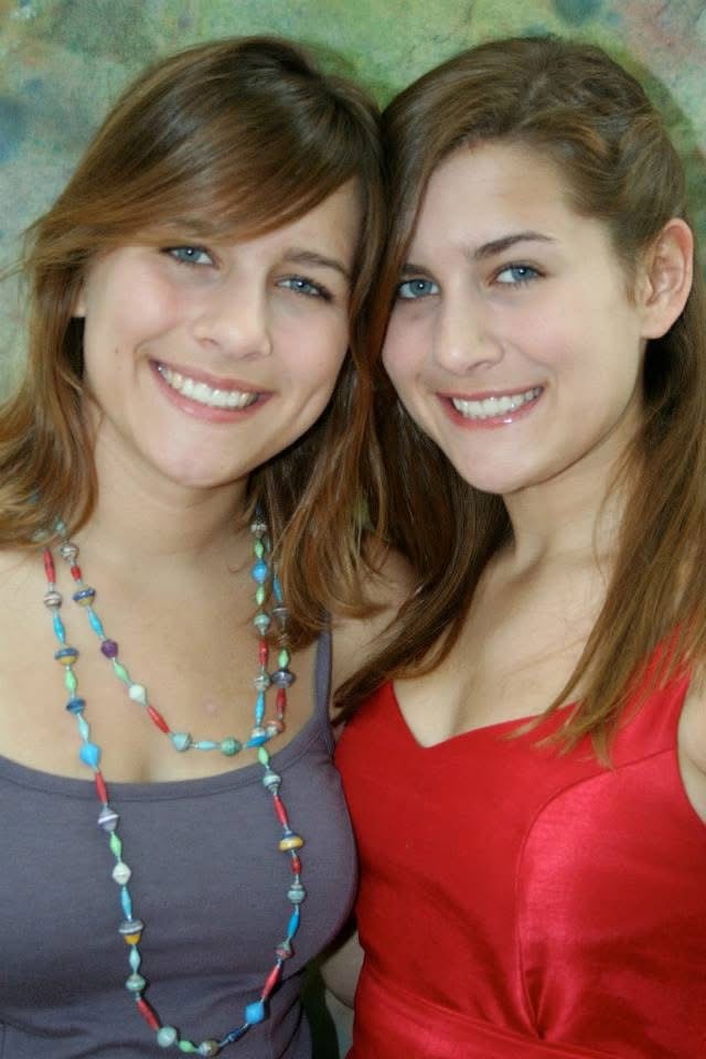 Two smiling women posing together against a colorful painted background