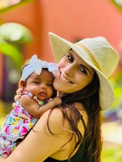 Woman in straw hat smiling and holding a baby in a colorful outfit