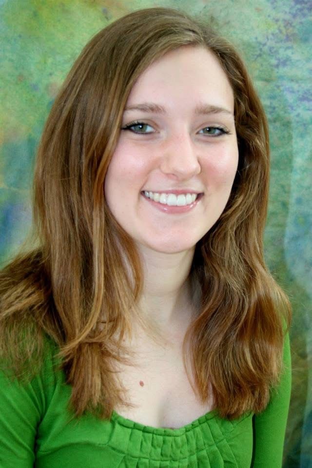 Young woman in green top smiling against a colorful painted background